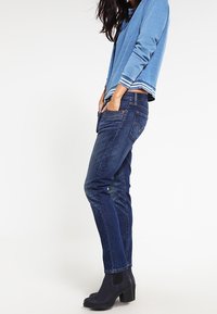 Blå sweatshirt med vita randiga ärmar, kombinerad med mörkblå jeans och svarta ankelboots. Outfitten är avslappnad och figurnära.