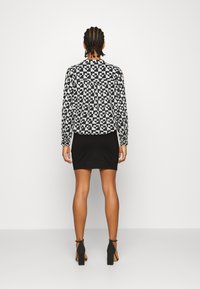 Blouse à motifs noir et blanc à manches longues, associée à une mini-jupe noire et des sandales à talons hauts. Coupe standard et design décontracté.