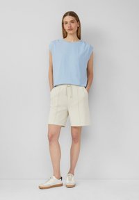 Top azzurro chiaro a maniche corte con un taglio morbido, abbinato a pantaloni corti bianchi con coulisse. Il modello indossa scarpe da ginnastica beige con dettagli testurizzati.