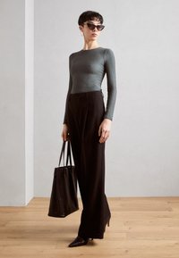 Graues, eng anliegendes Langarmoberteil, hochgeschnittene schwarze weite Hose, spitze schwarze Absätze und eine strukturierte schwarze Tragetasche.