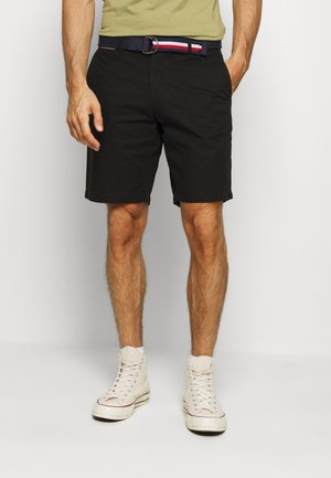 Pantalones cortos negros de algodón con un cinturón que presenta rayas azules, rojas y blancas, combinados con zapatillas altas color crema.