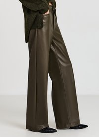 Weit geschnittene Hosen aus olivgrünem Kunstleder mit glatter Oberfläche, feinen Nähten und hoher Taille, kombiniert mit spitzen schwarzen Schuhen.