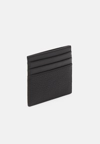 Porte-cartes en cuir noir avec une surface texturée, comportant quatre emplacements pour cartes d'un côté et une finition lisse de l'autre.