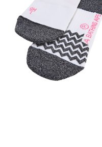Weiße Socken mit einem schwarzen gesprenkelten Zeh und Ferse. Das Design zeigt horizontale Streifen und ein Zickzackmuster. Roter Logo-Text ist sichtbar.