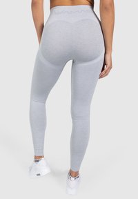Leggings grises de cintura alta con un material elástico, que presentan una cinturilla texturizada y detalles de moldeado en las piernas. Zapatillas blancas.