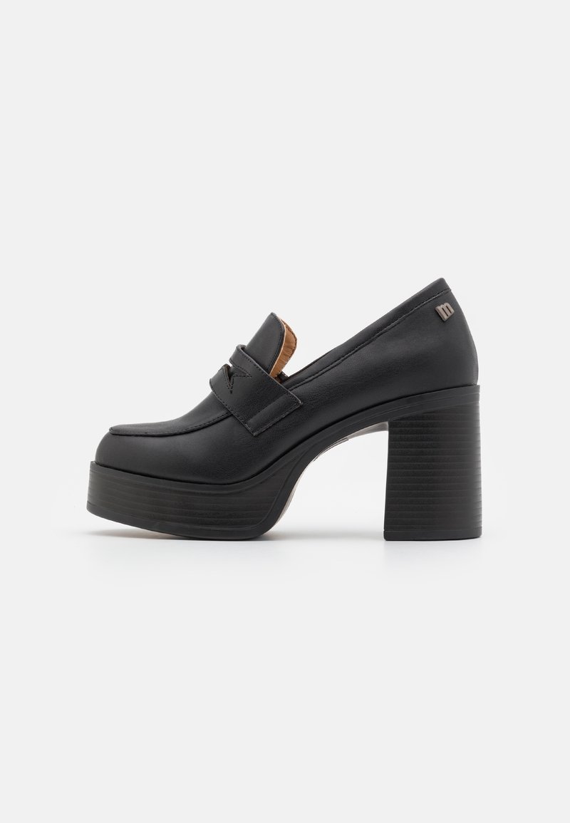 Mocassin plateforme noir à talon bloc haut et épais, dessus en cuir, avec détail de sangle, présenté en vue latérale sur fond blanc.