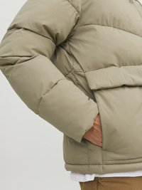 Puff jakke i lys beige, med en tekstureret overflade, polstret design og sidelomme. Kraven er høj og giver ekstra isolering.