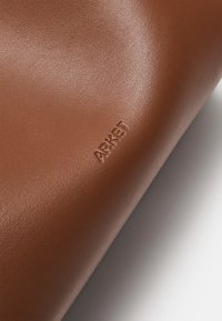Materiale in pelle marrone con una texture liscia, caratterizzato da un discreto logo impresso "ARKET". L'oggetto ha una forma rettangolare con angoli arrotondati.