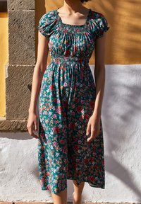 Sukienka w kwiaty z krótkimi bufiastymi rękawami, wykonana z lekkiego materiału. Zielona baza z żywymi różowymi i pomarańczowymi kwiatami, z marszczonym w talii pasem.