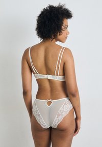 Set de lenjerie albă care include un sutien cu bretele subțiri și un spate decorat cu dantelă, asociat cu chiloți cu talie înaltă asortați, cu margine din dantelă și detalii cu decupaje.