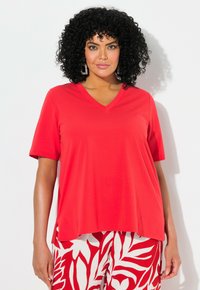 Rode V-hals t-shirt met korte mouwen, gemaakt van zachte stof, met een losse pasvorm die tot op de heup reikt. Gecombineerd met geblokte witte en rode broek.
