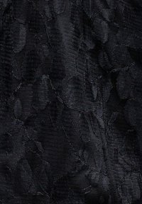 Nærbillede af sort stof med subtilt blomsterblonde mønster og teksturerede vævede detaljer.