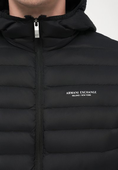 Doudoune noire avec fermeture éclair, dotée d'une capuche et d'un design matelassé horizontal. Logo de la marque "Armani Exchange" en blanc sur la poitrine.