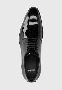 Zwarte gepatineerde leren veterschoen, spitse neus, vetersluiting, glad oppervlak, binnenkant toont merknaam, minimalistische stijl.