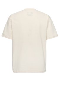 Camiseta de algodón color crema con mangas cortas y cuello redondo. Presenta una parte trasera lisa y un sutil logo en el centro superior.