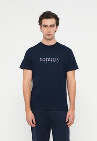 Tricou din bumbac de culoare bleumarin, cu un print grafic ce afișează "tommy" în culori vibrante și "JEANS" dedesubt. Design clasic cu guler rotund.