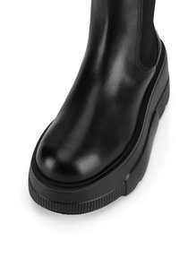 Czarny skórzany botek za kostkę o gładkiej powierzchni, zaokrąglonym nosku, elastycznych bocznych panelach i grubej, teksturowanej podeszwie.
