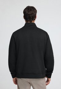 Schwarzer Sweatshirt mit hohem Kragen, aus strukturiertem Stoff gefertigt. Verfügt über gerippte Bündchen und Saum. Sauberes, simples Design ohne Verzierungen.