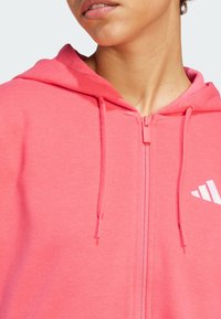 Rosa zip-up hettegenser med en myk tekstur, med hette, hvit logo på brystet, og matchende snorer for justering.