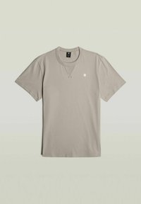 Camiseta de manga corta gris claro de algodón, con cuello redondo y un pequeño logo en el lado izquierdo del pecho. Textura suave.