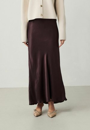 Gonna satin lunga e scura color bordeaux con una silhouette fluente, indossata con un cardigan aderente color crema con bottoni dorati.