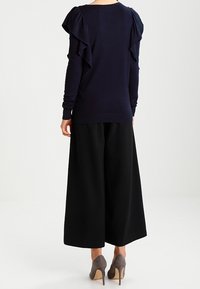 Maglione della marina con dettagli arricciati sulle spalle, abbinato a pantaloni larghi neri. La modella indossa tacchi alti color taupe. Texture morbide in tutto l'outfit.