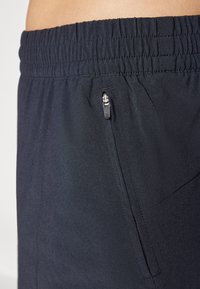 Los pantalones cortos atléticos negros cuentan con una cintura elástica y un bolsillo lateral con cremallera. La tela parece suave y ligera.