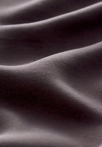 Tessuto scuro con una consistenza morbida e levigata e una lucentezza sottile, che mostra pieghe e curve delicate in diverse tonalità di grigio carbone intenso.