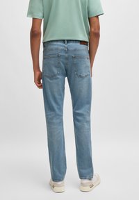 Jeans azul claro com um design clássico de perna reta, com bolsos traseiros e detalhes de costura, combinados com uma camisa de manga curta verde menta.