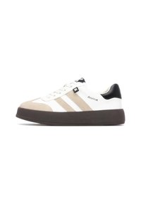 Zapatilla blanca con acentos en beige y negro. Presenta una puntera de ante, un diseño de tres rayas y una gruesa suela de caucho negro.