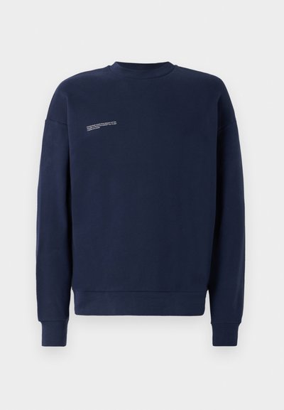 Tums zilas kreklu jaka, kas izgatavota no mīkstas auduma, ar apaļu kaklu, garām piedurknēm un nelielu baltu teksta detaļu priekšpusē.