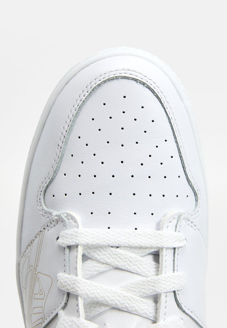 Sneaker bianca in pelle con punteggiatura sulla punta, lacci bianchi piatti e una texture liscia. Presenta un branding minimo sul lato.