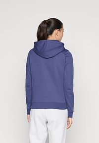 Navy blue hooded sweatshirt with a soft texture, ribbed cuffs, and hem, viewed from the back, paired with light gray sweatpants.