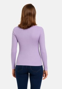 Maglione a maniche lunghe di colore viola chiaro, caratterizzato da una texture a coste e un design aderente. Abbinato a pantaloni blu scuro.