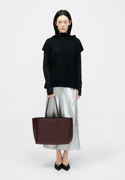 Σκούρο μπορντό δερμάτινη τσάντα tote με δύο μακριές χειρολαβές και διακριτικό ανάγλυφο λογότυπο, συνδυασμένη με μαύρο φούτερ με κουκούλα και ασημένια φούστα.