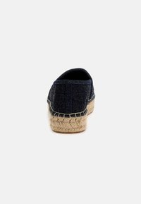 Navy denim espadrille with a woven jute sole. Features a rounded back and contrasting stitched accents along the edge. Simple and casual design.
