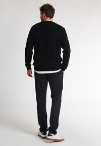 Maglione nero a maglia con colletto rotondo, abbinato a pantaloni neri a sigaretta e sneakers bianche. Tessuto testurizzato, design comodo.