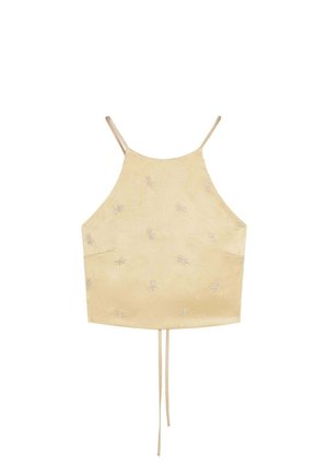 Top corto beige con tirantes finos y un sutil patrón floral bordado, con cordones que cuelgan del centro inferior.