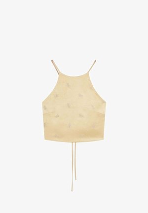 Crop top beige con spalline sottili e motivo floreale ricamato discreto, con stringhe annodabili che pendono dal centro in basso.