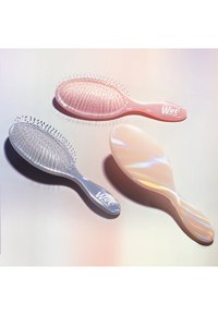 Drie haarborstels: één doorzichtige, één roze en één parelmoer, allemaal met flexibele haren en ergonomische handvatten, met het logo "Wet Brush".