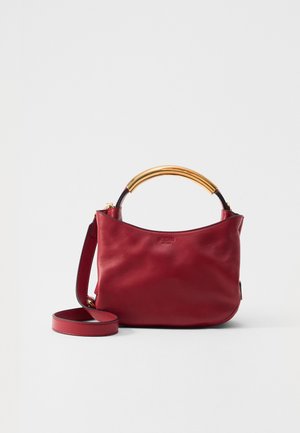 Sac à main en cuir rouge avec une poignée incurvée en doré et une bandoulière réglable, présentant une texture lisse et un design minimaliste.