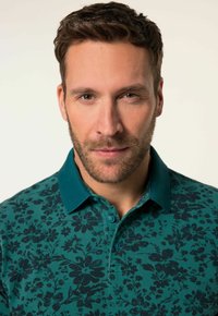 Zelené polo tričko s tmavým květinovým vzorem, kontrastním límečkem a dvěma knoflíky. Hladká textura, krátké rukávy, přiléhavý střih.