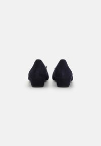 Scarpe in suede blu scuro con tacco basso e quadrato e punta arrotondata. La parte posteriore presenta un design semplice senza hardware o accenti visibili.
