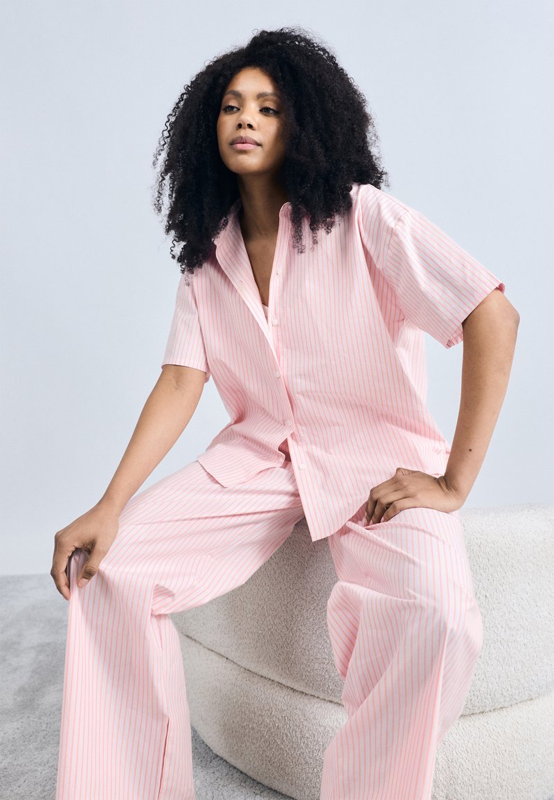 Ροζ ριγέ πουκάμισο με κοντά μανίκια και αντίστοιχο παντελόνι φαρδιάς γραμμής από ελαφρύ ύφασμα, με άνετη εφαρμογή και διακριτική λάμψη.