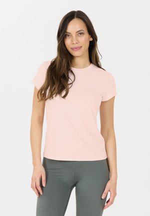 Helles rosa kurzärmliges, eng anliegendes T-Shirt mit Rundhalsausschnitt, aus einem glatten Stoff gefertigt, kombiniert mit hoch taillierten dunkelgrünen Leggings.