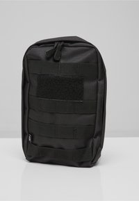 Bolsa táctica compacta negra con múltiples correas horizontales y un parche de gancho y bucle en el frente, colocada en posición vertical sobre una superficie blanca.