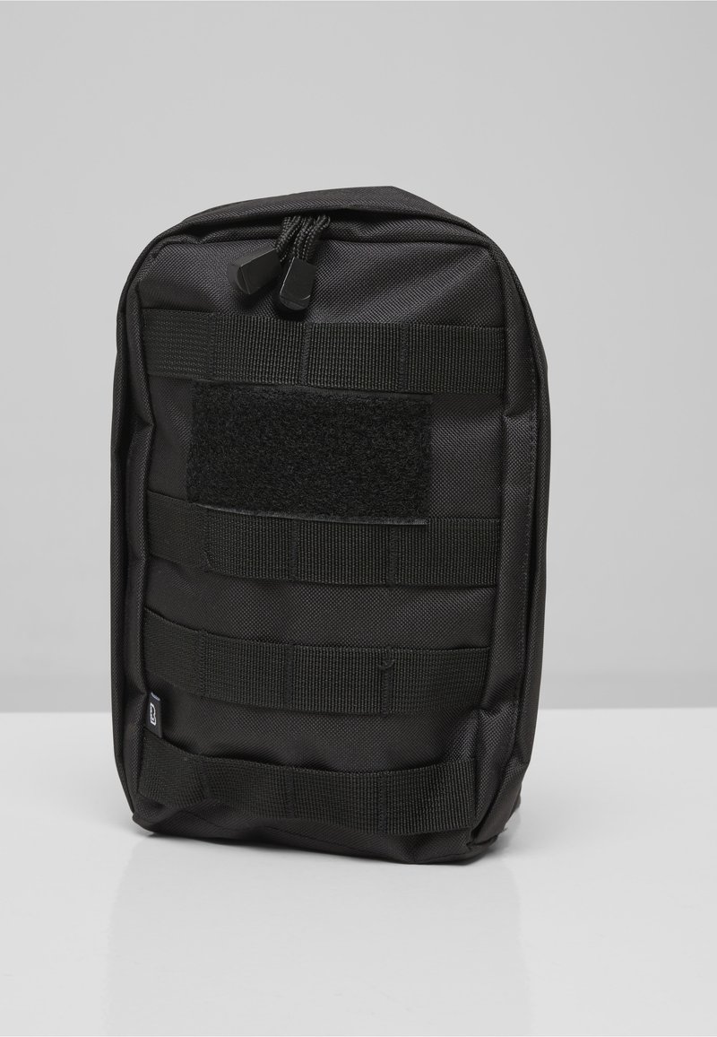 Bolsa táctica compacta negra con múltiples correas horizontales y un parche de gancho y bucle en el frente, colocada en posición vertical sobre una superficie blanca.