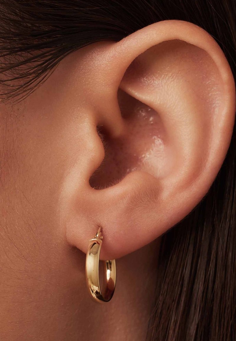 Boucle d'oreille en or, petite et lisse, présentée dans une oreille percée. La boucle d'oreille possède une surface brillante et une forme simple et arrondie.