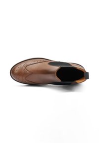 Botín de cuero marrón con un acabado suave, paneles laterales elásticos, perforaciones decorativas y una suela negra delgada.