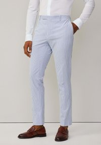Pantaloni a righe blu chiaro realizzati in tessuto con una texture liscia, caratterizzati da una vestibilità slim e frontale piatto. Indossati con scarpe in pelle marrone.